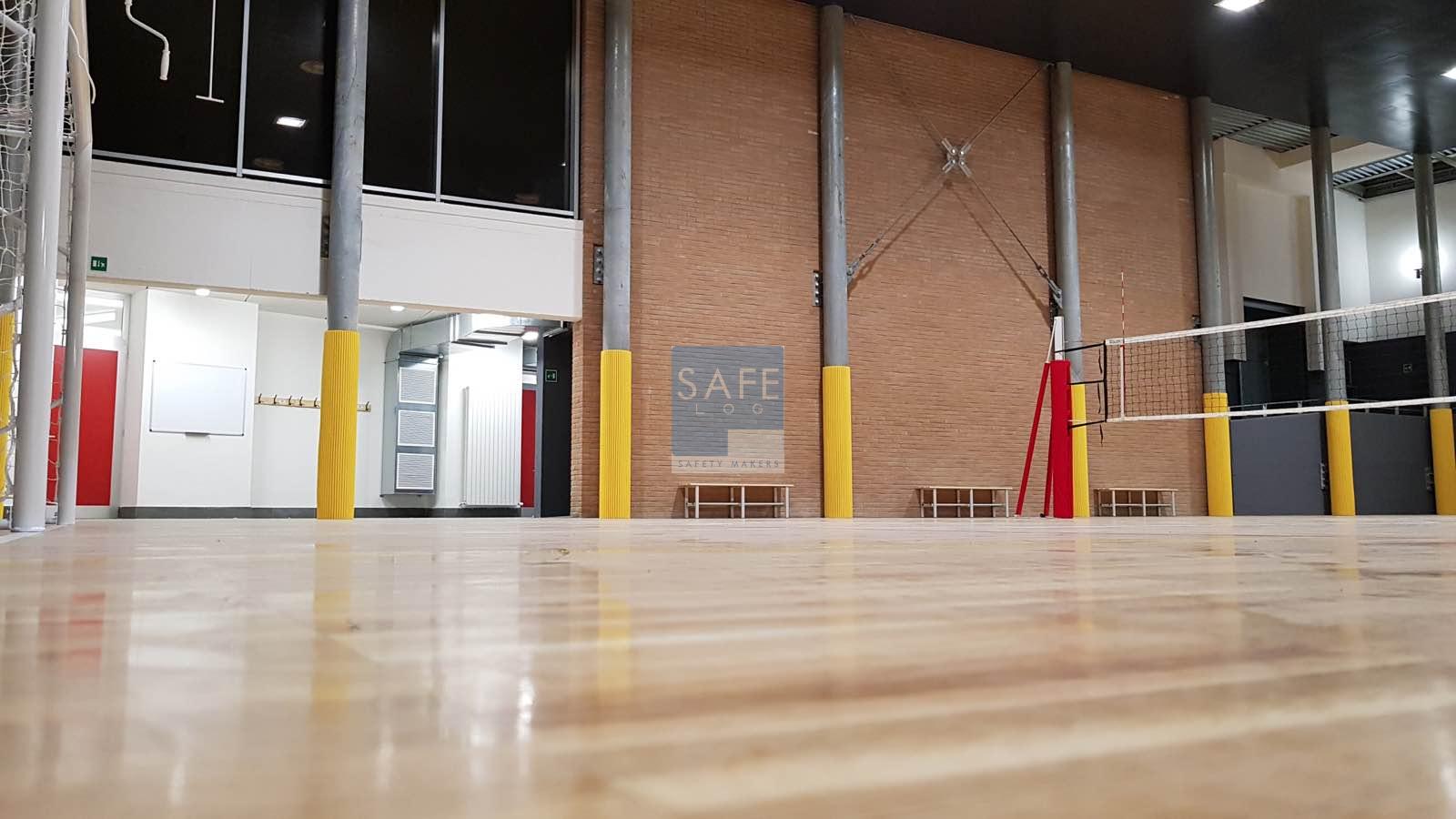 Installazione di pannelli in gomma antiurto su muro sotto canestro e colonne perimetrali in una palestra a Pistoia. Le protezioni in gomma gialla e grigia garantiscono sicurezza durante le attività sportive.