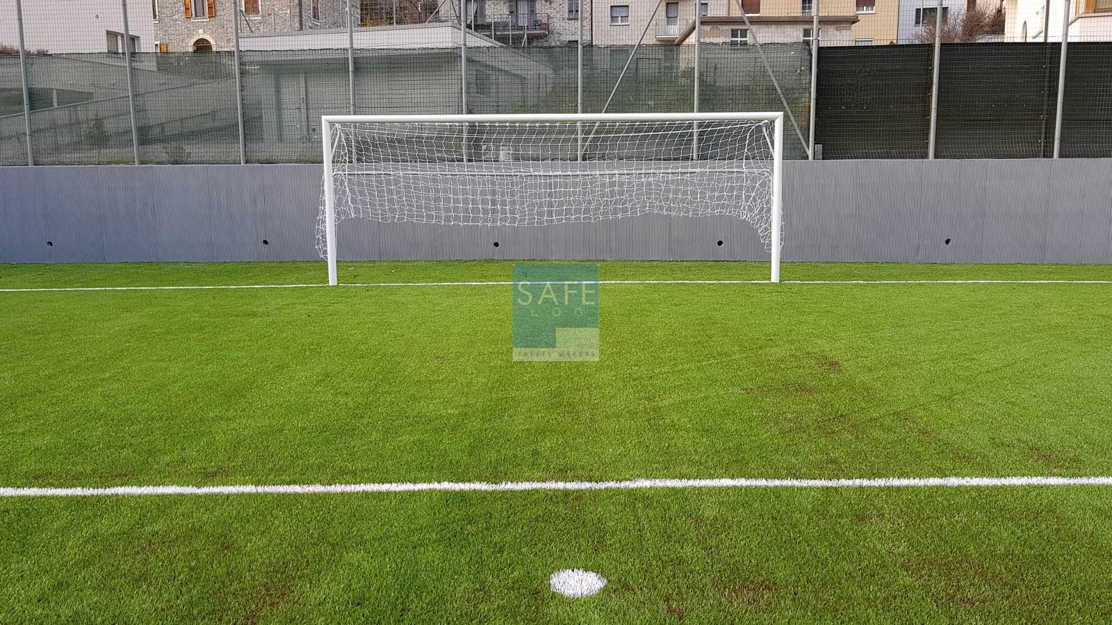 Pannelli antitrauma in gomma grigia Tetris installati verticalmente su muro perimetrale in calcestruzzo a bordo campo, con fori di scolo fresati a mano per garantire sicurezza e drenaggio